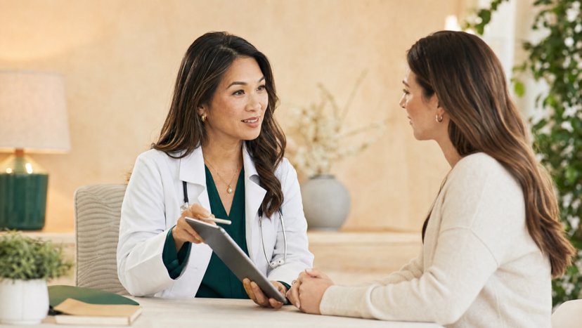 Clinician with a tablet talking with a patient across a desk
